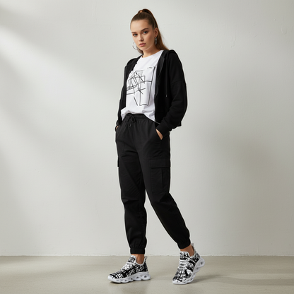Woman wearing a black cardigan, white graphic t-shirt, black cargo pants, and patterned shoes on a plain background