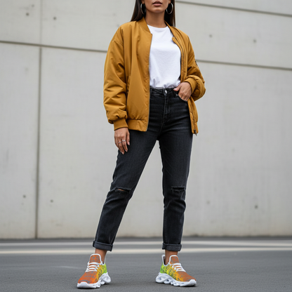Person wearing a mustard yellow bomber jacket, white shirt, black jeans, and colorful sneakers against a plain background.